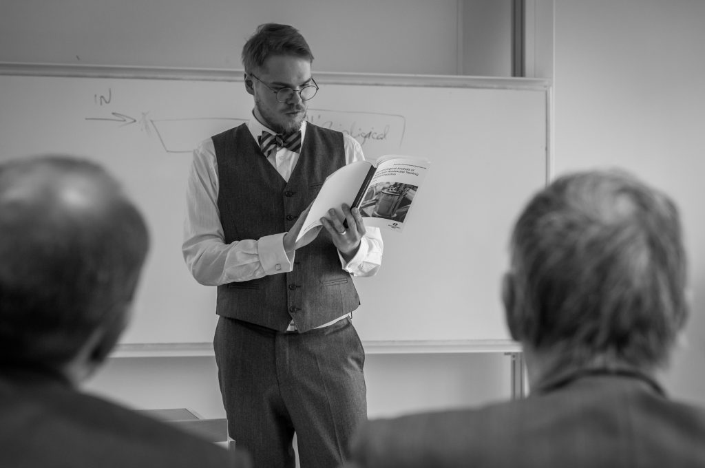 Ivo standing in front of a whiteboard looking at a book.